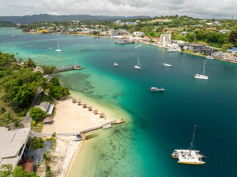 Aerial view of the turquoise waters meet the sandy shorelines, dotted with boats and buildings under a cloudy sky, Port Vila, Shefa Province, Vanuatu.