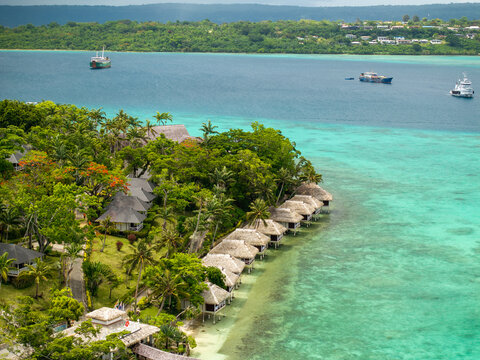 Aerial view of thatched bungalows line the turquoise coast, contrasting with the deep greens of the island's dense foliage, Port Vila, Shefa Province, Vanuatu.