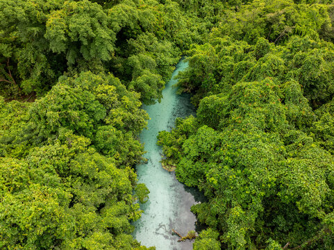 Aerial view of a bright blue river snaking through a dense, verdant jungle canopy, its waters reflecting the sky above, Espirito Santo, Sanma Province, Vanuatu.