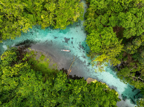 Aerial view of a solitary canoe glides through the crystalline turquoise waters of Blue Hole, framed by the emerald embrace of verdant rainforest, Espirito Santo, Vanuatu.