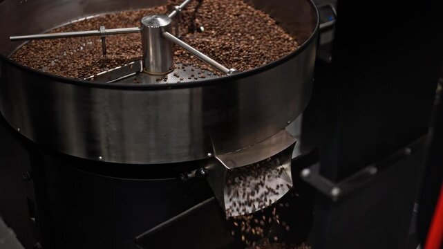 Slow motion view of roasted coffee beans cooling and moving inside an industrial cooling tray.Agitator rotates while excess beans exit the chute,marking a key stage of coffee production after roasting