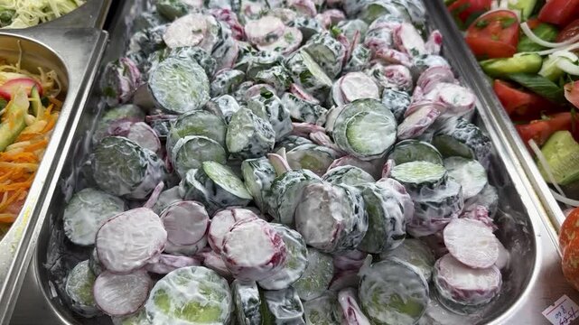 Fresh Cucumber Radish Salad On Tray Sour Cream Dressing Coats Sliced Cucumbers And Radishes With Tomato Wedges On Metal Baking Tray Arranged For Sale At Cafeteria Counter Vibrant Colors.