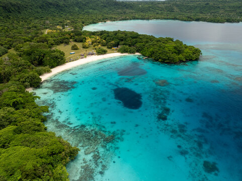 Aerial view of the vibrant turquoise waters gently caressing the pristine white sands, fringed by the lush green rainforest, Espiritu Santo, Sanma Province, Vanuatu.