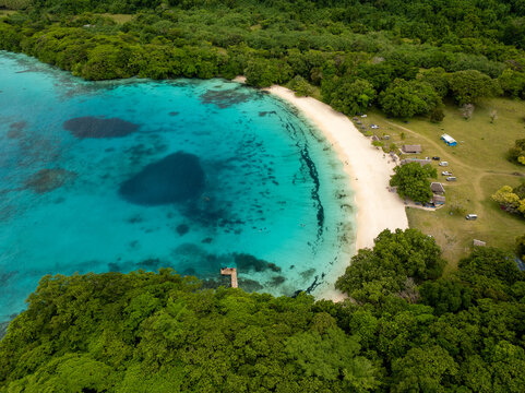 Aerial view of the vibrant turquoise waters gently embracing the pristine white sands, fringed by lush green trees, Espirito Santo, Sanma Province, Vanuatu.
