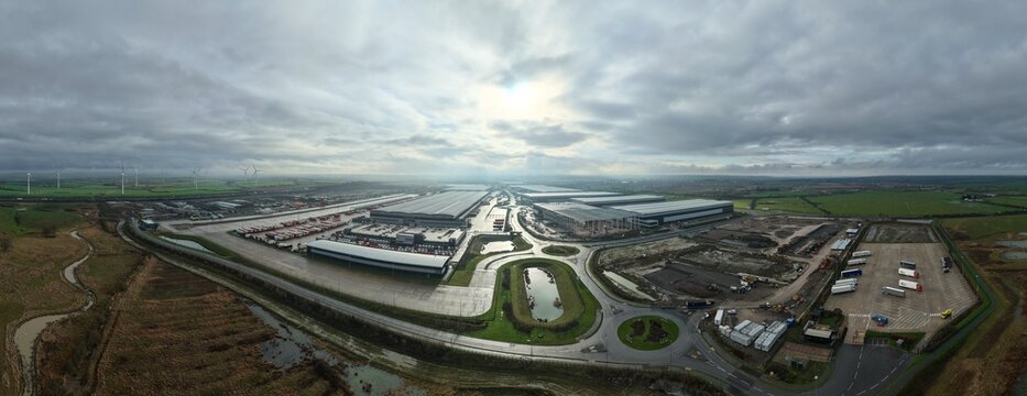 Aerial view of East Midlands Distribution Hub, where sleek, modern warehouses meet winding roads and verdant fields under a vast, textured sky, Crick, Northampton, United Kingdom.