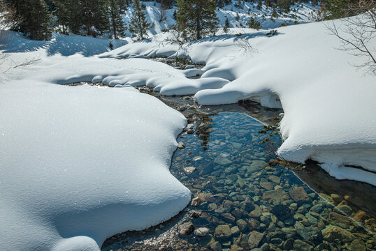 Clear stream flowing through deep snow.