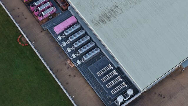 Aerial view of a sleek, modern data center with pink cooling systems neatly alongside, contrasting with the green lawn, Corby, United Kingdom.