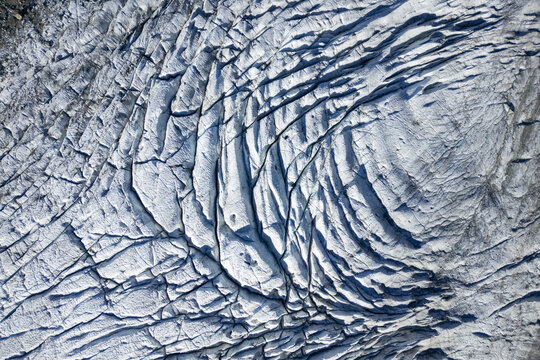 Aerial view of the intricate patterns etched into the icy expanse of Morteratsch Glacier, a frozen river winding through the Swiss Alps, Morteratsch Glacier, Grisons, Switzerland.
