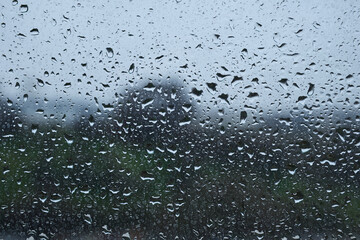 Raindrops on window with blurred landscape on a cloudy day