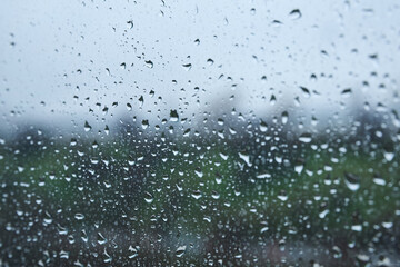 Raindrops on window with blurred landscape on a cloudy day
