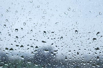 Raindrops on window with blurred landscape on a cloudy day