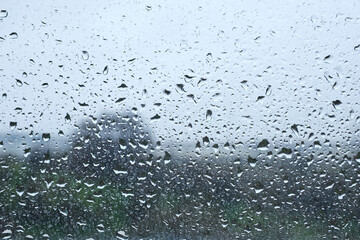 Raindrops on window with blurred landscape on a cloudy day