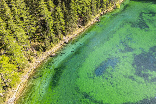 Aerial view of emerald waters meet the dense forest along the Gruner See shore, a vivid tapestry of nature's artistry, Green Lake - Gruner See, Styria, Austria.