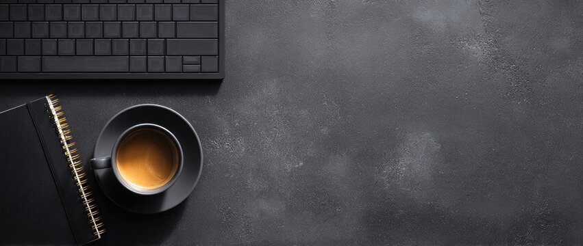 A dark, textured desk hosts a keyboard, notebook, and a cup of coffee. Modern workspace setup