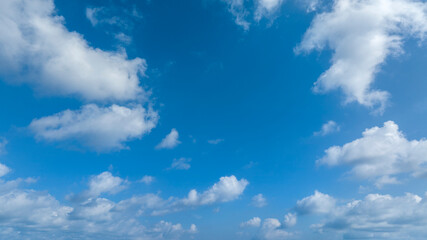 Obraz premium Wide-angle view of a bright blue sky filled with scattered white fluffy clouds. The daylight is soft and even across the entire sky.