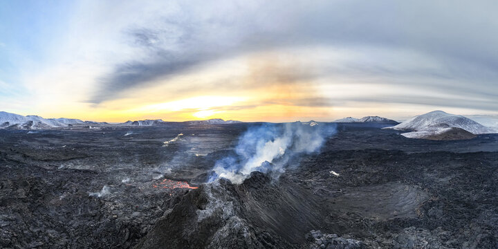 Aerial view of fiery lava erupts from a volcanic fissure, contrasting against the stark, snow-dusted landscape under a vibrant sky, Reykjavik, Iceland.