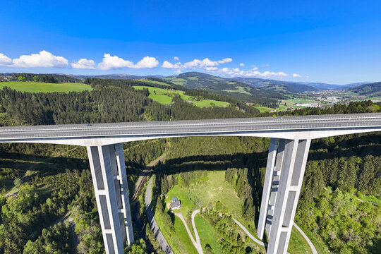 Aerial view of a colossal bridge piercing through a lush valley, connecting verdant hills under a radiant blue sky, Wolfsberg, Carinthia, Austria.