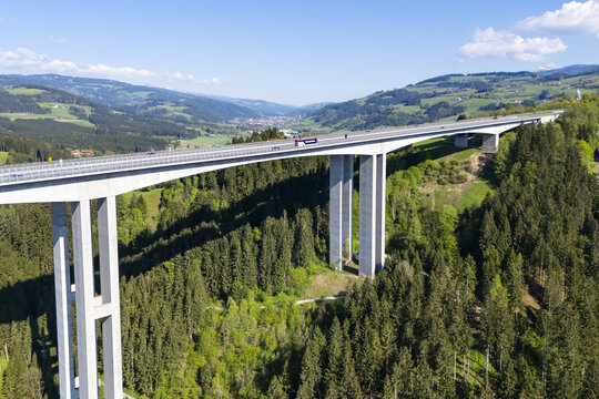 Aerial view of a modern bridge slicing through the verdant Lavanttal valley, its concrete pillars contrasting with the dense forest, Wolfsberg, Carinthia, Austria.