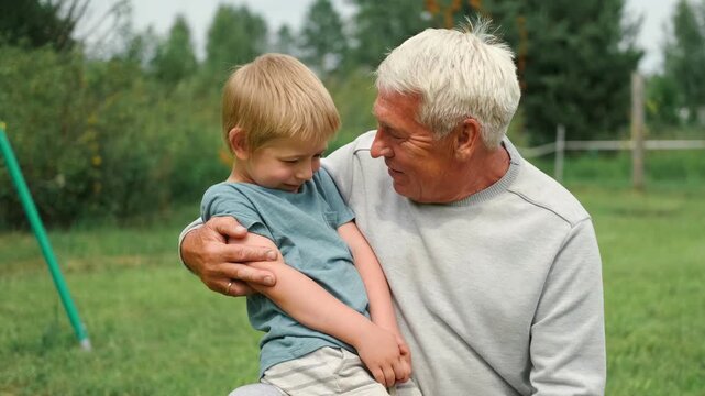 Grandfather and grandchild baby have fun during walk In Park. Happy family time. Old man grandpa hugging 4 years child boy at summer day. Smiling Senior male spending time with his grandson together.