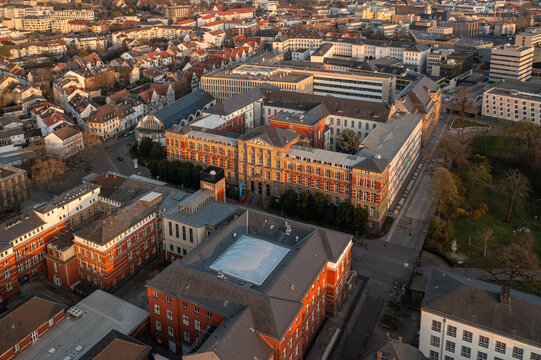 Aerial view of the grand Technische Universitat Darmstadt, its red-brick facade glowing under the sun's warm embrace, a stark contrast to the city's modern structures, Darmstadt, Hessen, Germany.