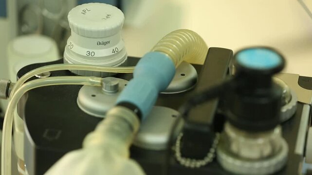 Close-up view of a medical anesthesia machine ventilator in a hospital operating room. The breathing bag inflates and deflates rhythmically, providing life support and oxygen during surgical procedure