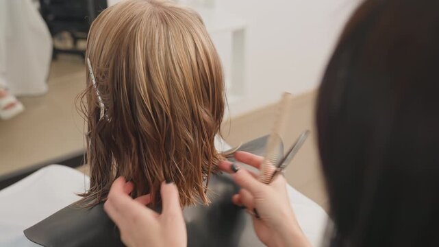 wet braided bob being trimmed by careful stylist, hands sectioning textured braids with comb and scissors over black cape in bright modern salon, closeup on precision cutting and finishing details,