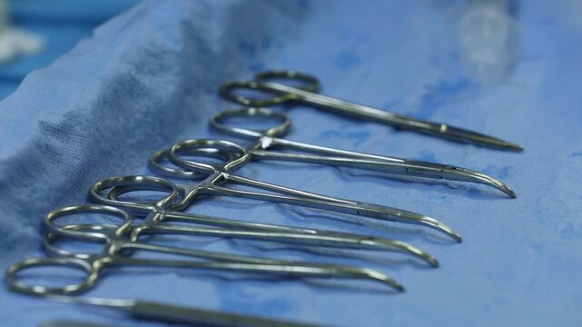 Close-up of shiny stainless steel surgical instruments arranged neatly on a blue sterile drape. Essential medical tools prepared for an operation in a hospital operating room environment.

