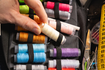 Une main sélectionnant une bobine de fil blanc dans une trousse de couture. © Gautier Normand