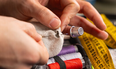 Une personne en train de réparer un trou dans une chaussette avec une aiguille, du fil et un dé à coudre. En arrière plan, une trousse à couture avec des bobines de fil. © Gautier Normand