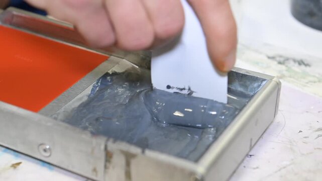 A man's hand mixes the ink in a silkscreen printing box in the workshop of a printing company