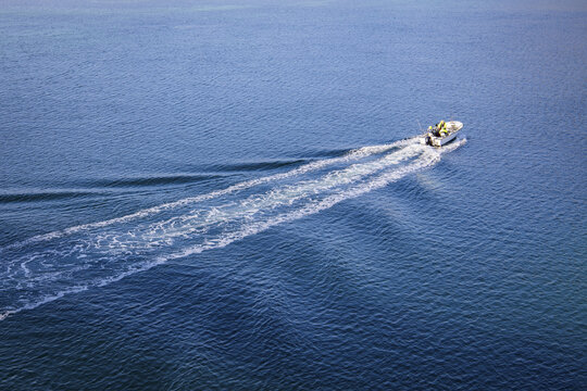 Aerial view of a boat speeding through the serene, deep blue waters, leaving a trail of white foam in its wake, Henningsvaer, Nordland, Norway.