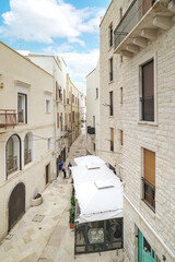 Bari, Italy. View of Vico X Corsioli from Via Venezia in Bari, showing narrow stone buildings and a historic alley perspective, with the ancient Palazzo del Sedile tower visible in the distance.