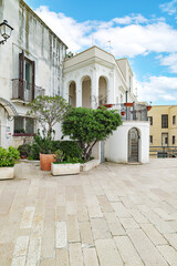 Bari, Italy. Facade of historic buildings and homes along Via Venezia in Bari, with light stone walls, arches, balconies and potted plants in a quiet pedestrian setting. Vertical image.