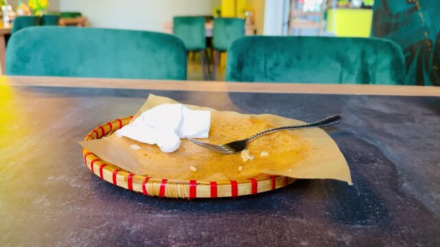 Used Paper Napkin And Fork On Plate, Visible Grease Marks And Crumbs On Woven Charger, Warm Sunlight And Textured Surface, Casual Cafe Aftermath During Barista Break, Inviting Cozy.