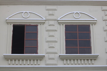 Classical architectural detail of symmetrical windows with pediments and decorative moldings on a cream building facade © Yeniceri
