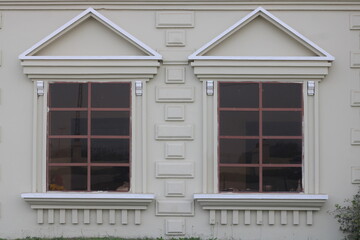 Classical architectural detail of symmetrical windows with pediments and decorative moldings on a cream building facade © Yeniceri