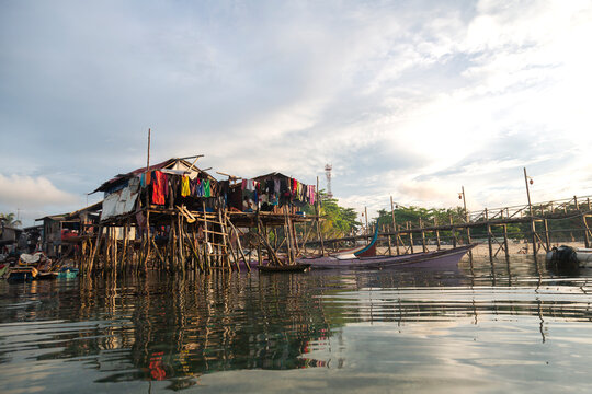 Homes on stilts by the water at sunset with clothes hanging out to dry and fishing boats nearby on Mabul island in Malaysia
