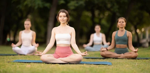Fotobehang Ontspanning Group of young women doing yoga lotus pose on mat in park  © JackF