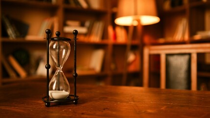 Hourglass on a wooden table in a library with warm lighting and bookshelves © shine.graphics