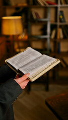 Naklejka premium Person in suit holding an open bible in a library with bookshelves in the background