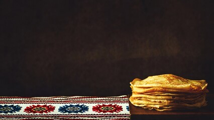 Traditional stack of homemade pancakes on embroidered folk textile with copy space representing national cuisine and cozy comfort food concept
