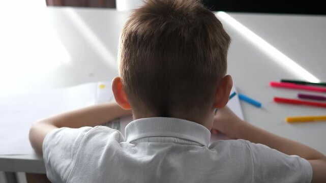 Close-up of a young boy writing or drawing with a pencil at a desk at home or school. Child focused on learning and doing homework. Concept of education, childhood development, concentration