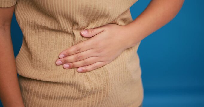 Sick woman holding belly, having stomach pain, diarrhea selective focus on hands on blue background