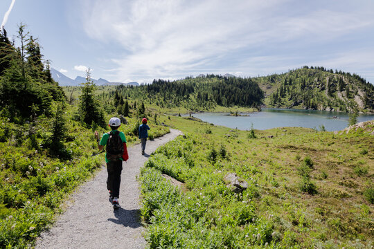 Two young boys walking along a trail in nature with a lake and green nature all around