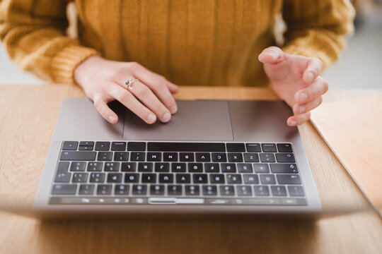A person wearing a yellow sweater uses a laptop, their hands resting on the keyboard and trackpad.
