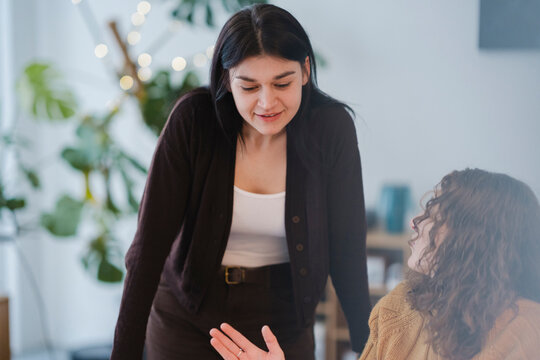 Two women are engaged in a conversation, one leaning forward attentively while the other listens with a smile.