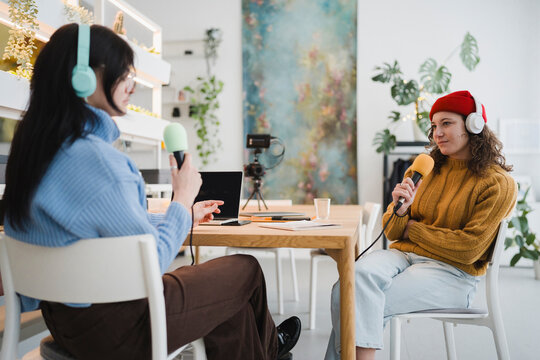Two young women wearing headphones are recording a podcast interview at a table with microphones and a laptop.