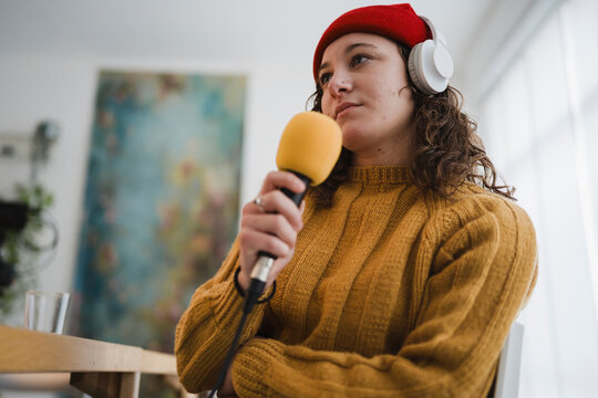 A young woman wearing headphones and a red beanie holds a microphone, ready to record her podcast or broadcast.