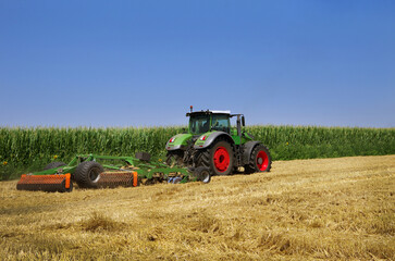 agricultural tractor working in the field after harvesting wheat next to a cornfield