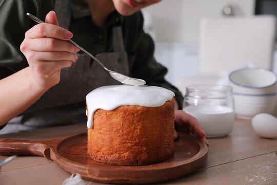 Young woman decorating traditional Easter cake with glaze in kitchen, closeup